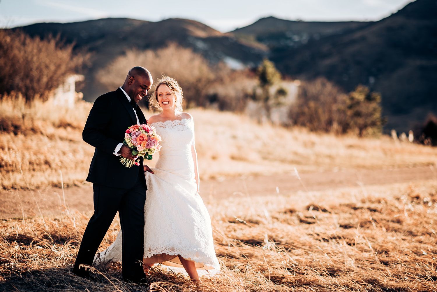Wedding couple walking together on sunlit mountain terrain with bouquet.
