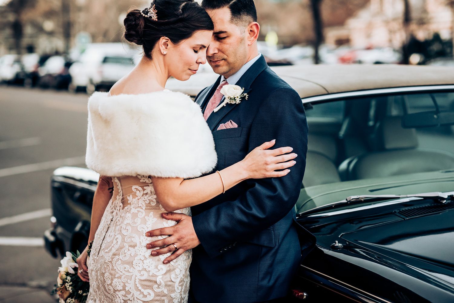 Intimate wedding moment captured beside classic car with winter fur wrap.