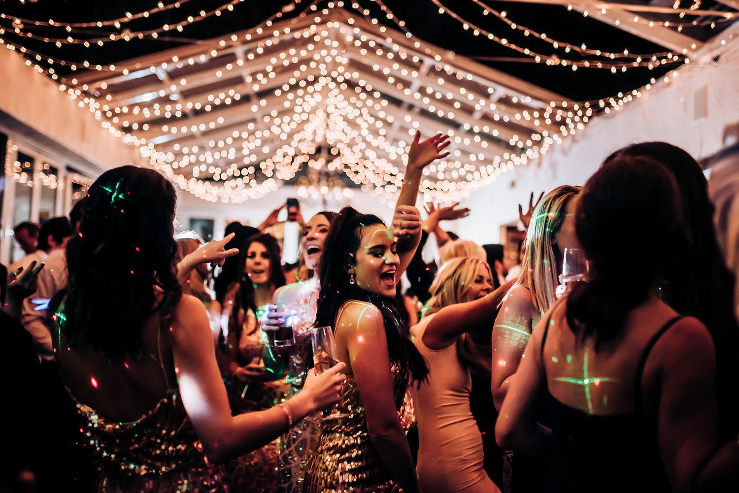 Lively dance party scene with string lights overhead at an indoor reception venue.
