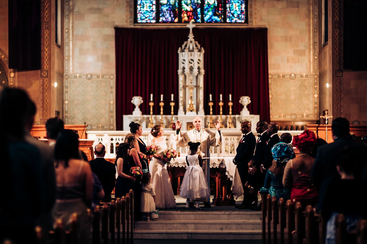 Wedding ceremony takes place at an ornate church altar with candles and stained glass windows.