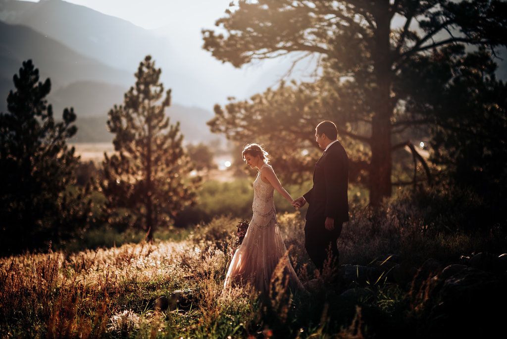 Couple walks through sunlit mountain landscape during golden hour.