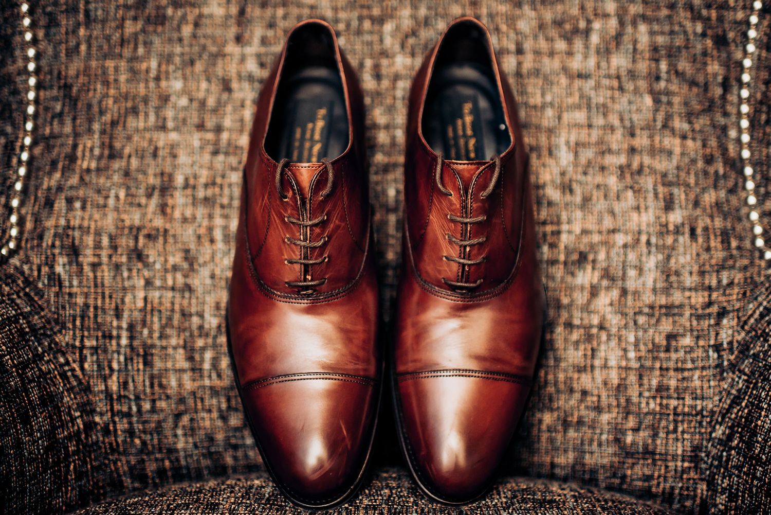 A pair of polished brown leather oxford dress shoes displayed on textured fabric.