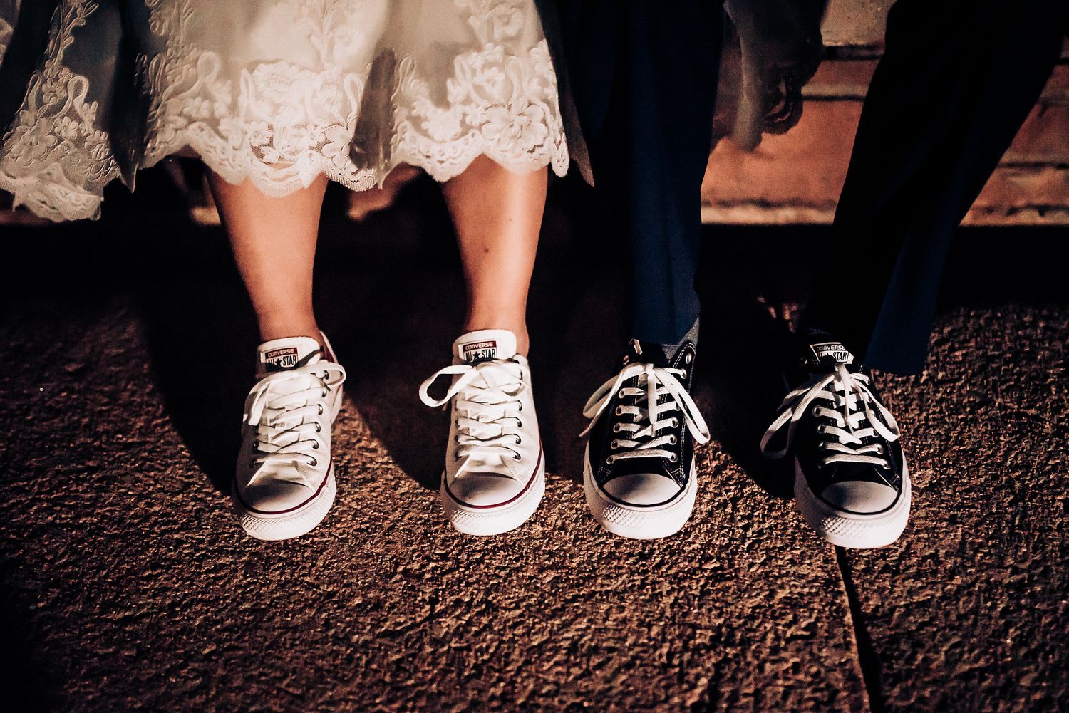 Black Converse sneakers worn with formal attire showing beneath a lace dress hem.