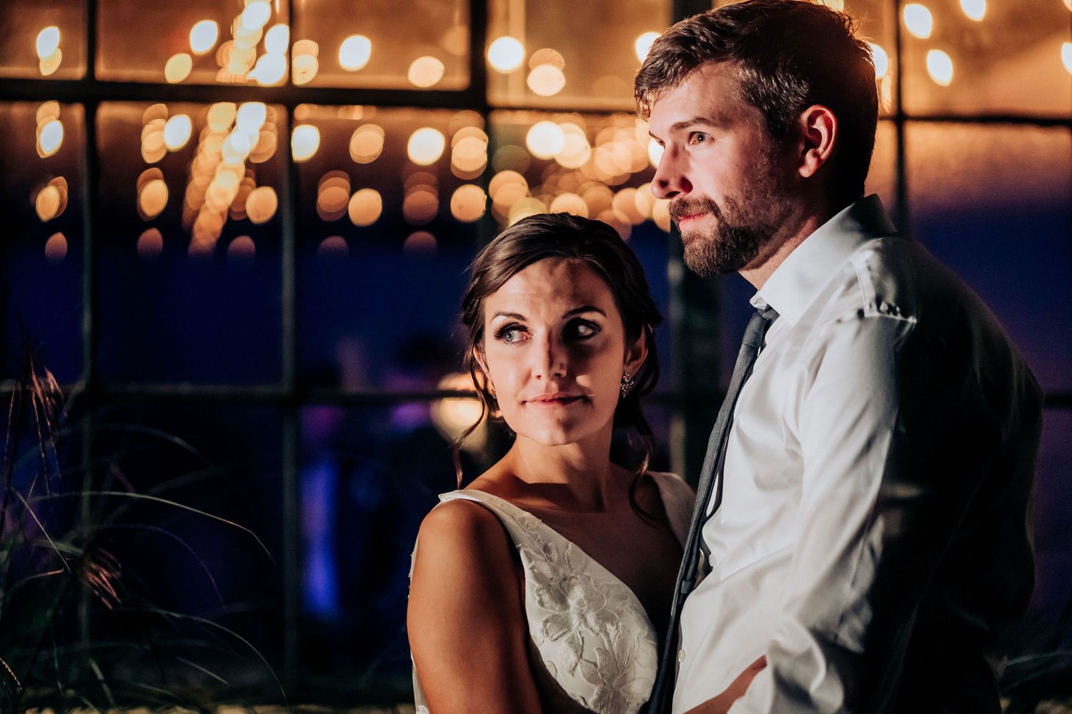 A romantic indoor wedding portrait silhouetted against glowing bokeh lights in an evening setting.