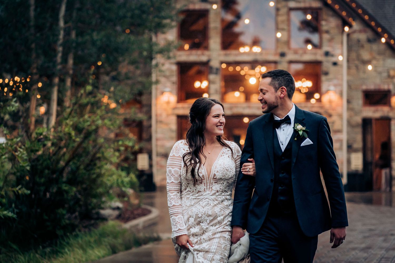 Happy couple walking together outside rustic lodge with twinkling lights.
