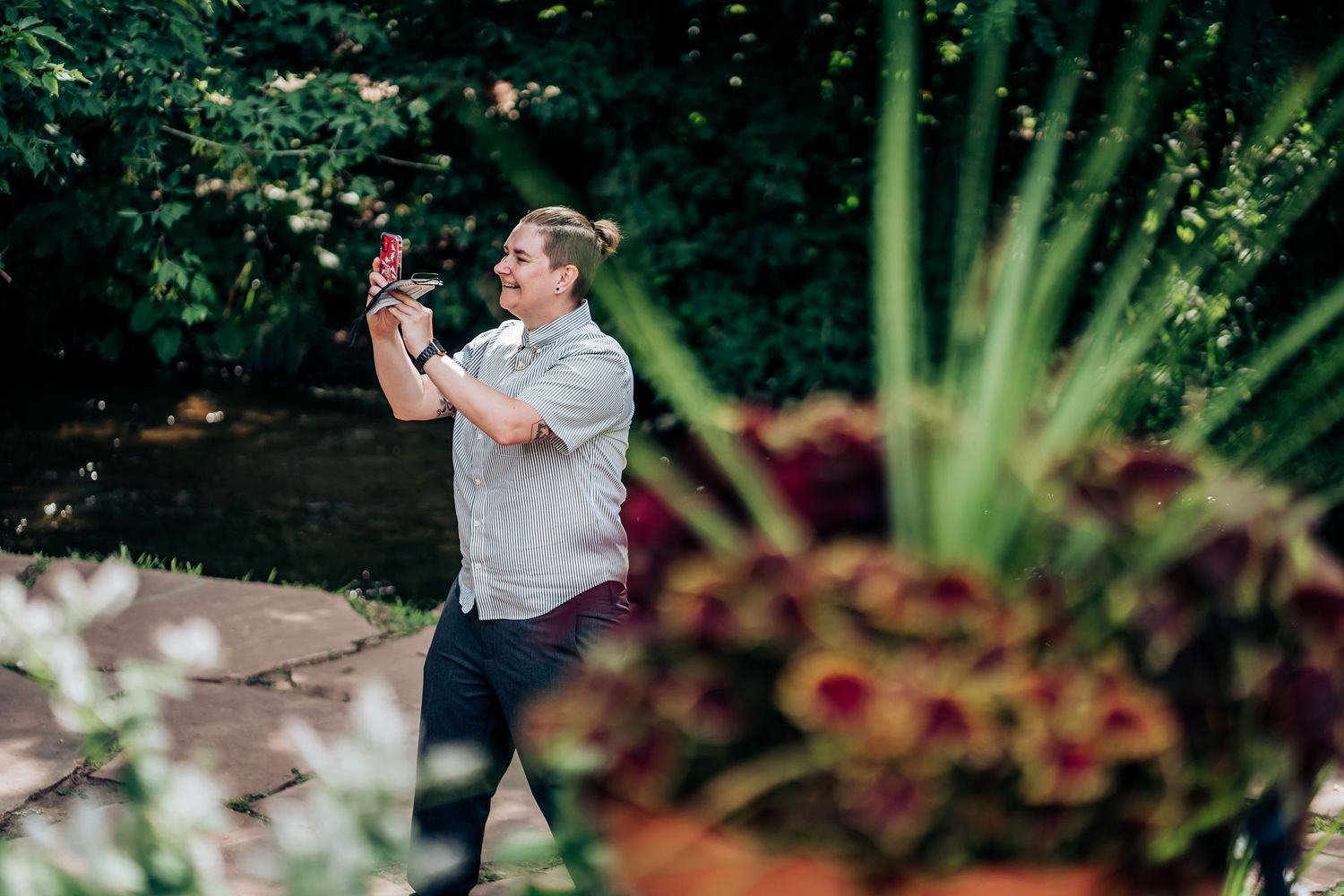 Person in grey shirt joyfully dancing outdoors surrounded by greenery.