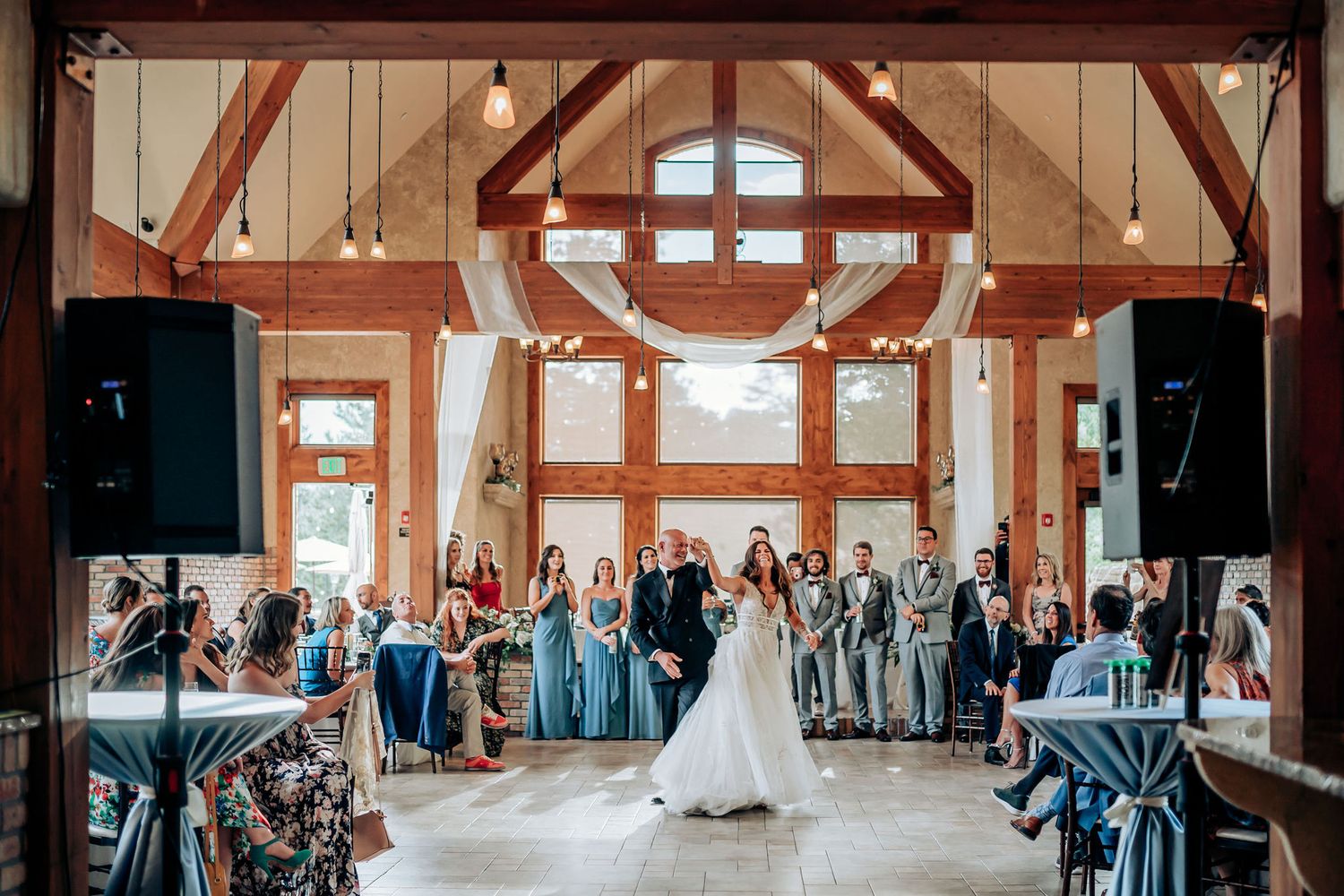 Wedding celebration in a barn-style venue with exposed beams and large windows.