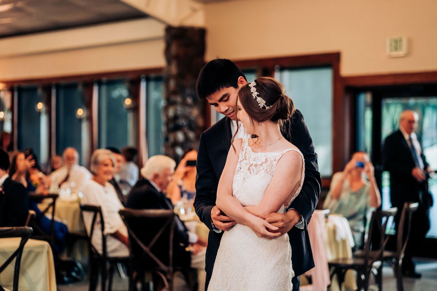 A romantic slow dance moment during a wedding reception with guests watching in the background.