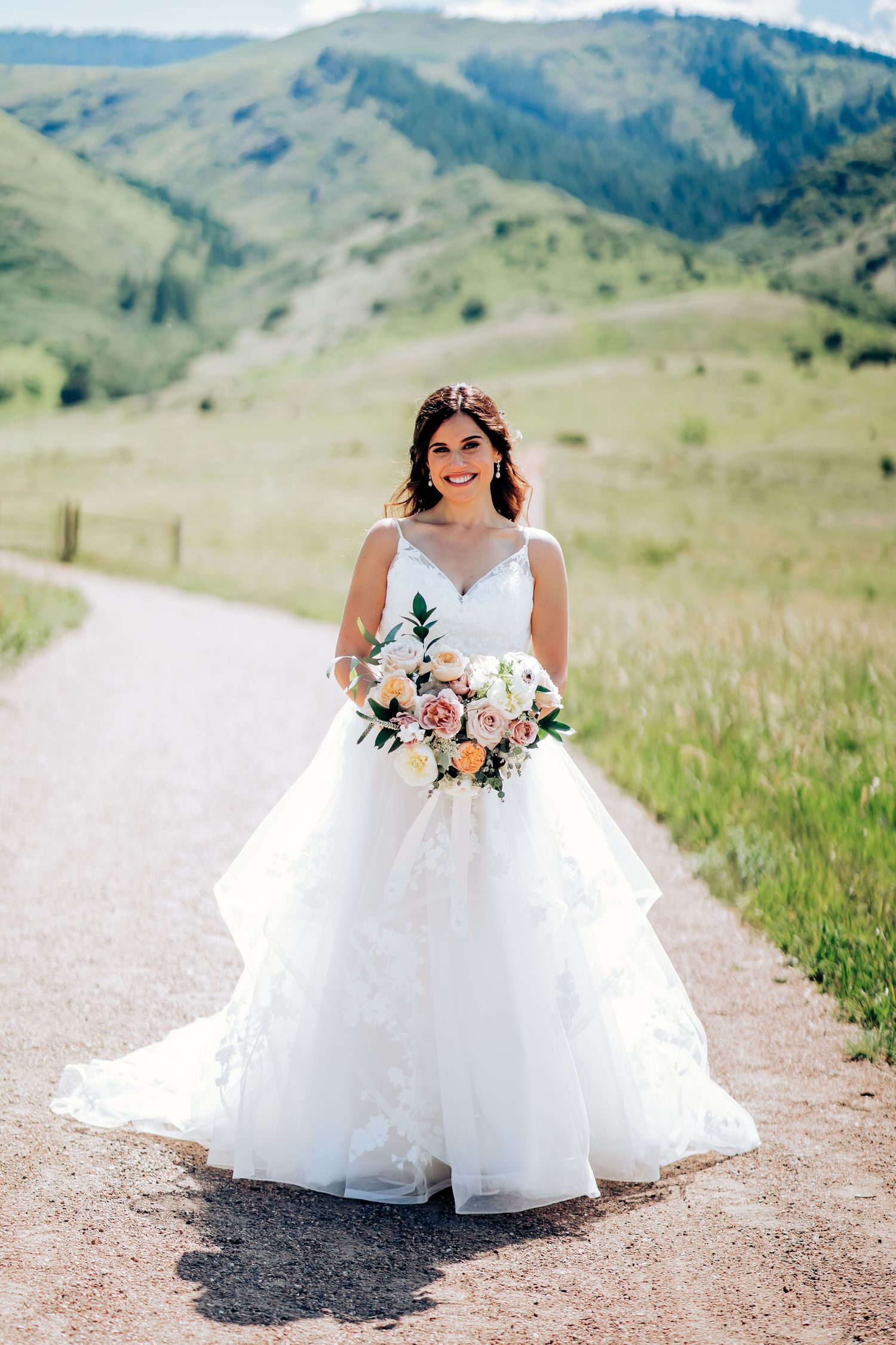 A bride in a white ball gown poses on a mountain path with rolling hills in the background.