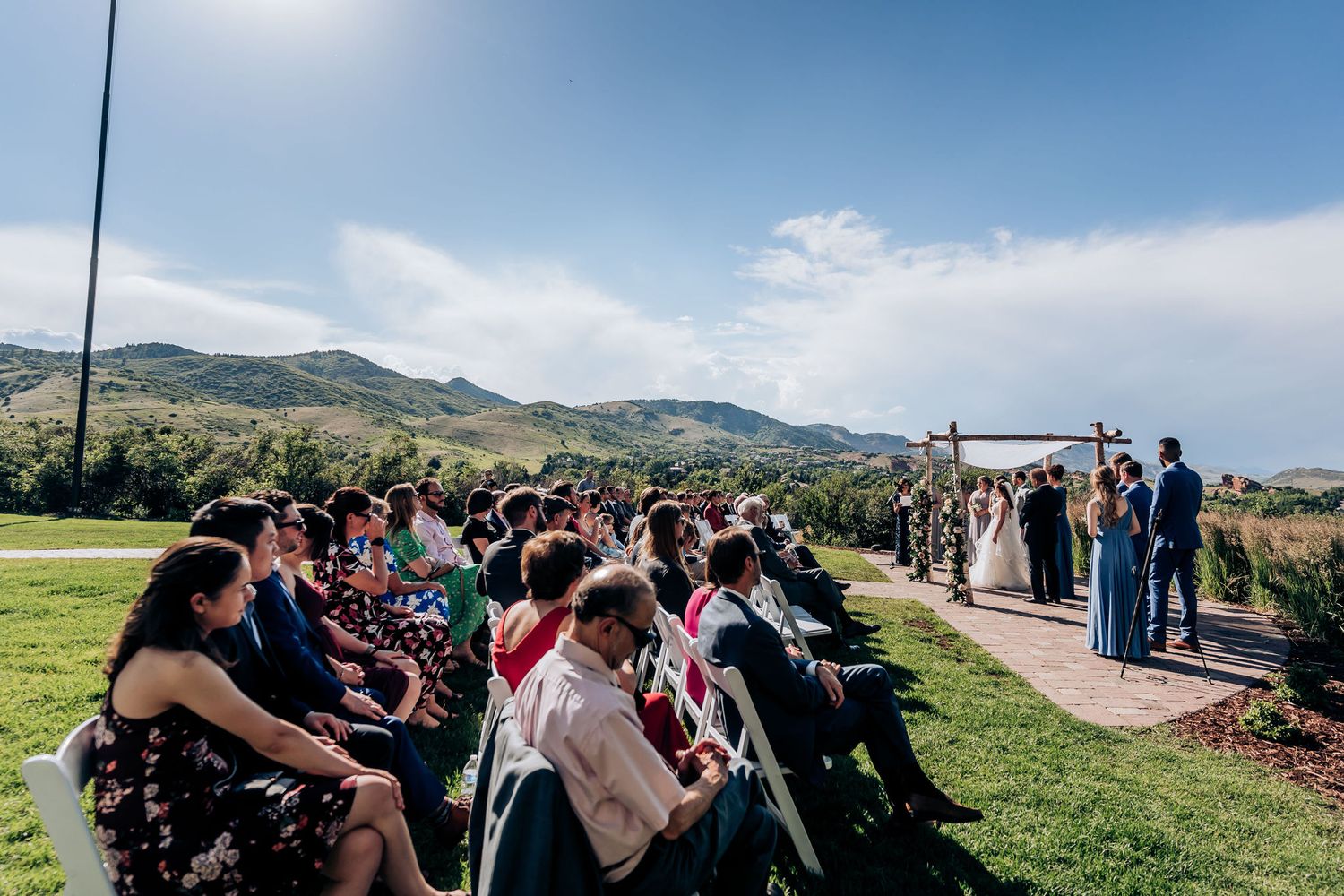 Wedding guests seated on chairs during an outdoor mountaintop ceremony with rolling hills in the background.