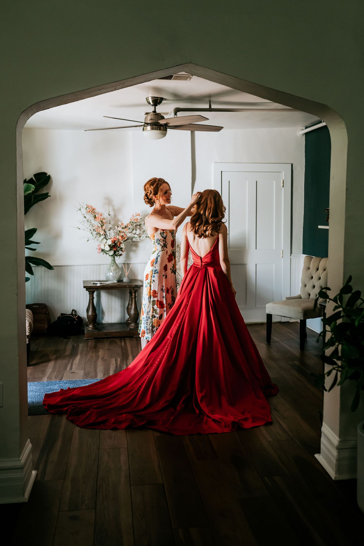 A stunning red ball gown being adjusted in an elegant white-walled room.