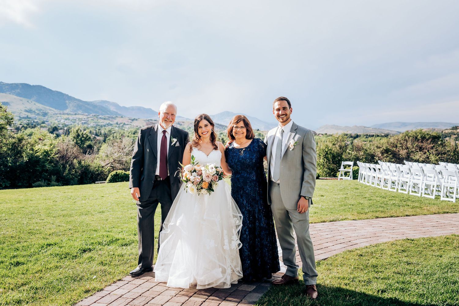 Wedding party poses together on a hilltop lawn with mountains in the background.