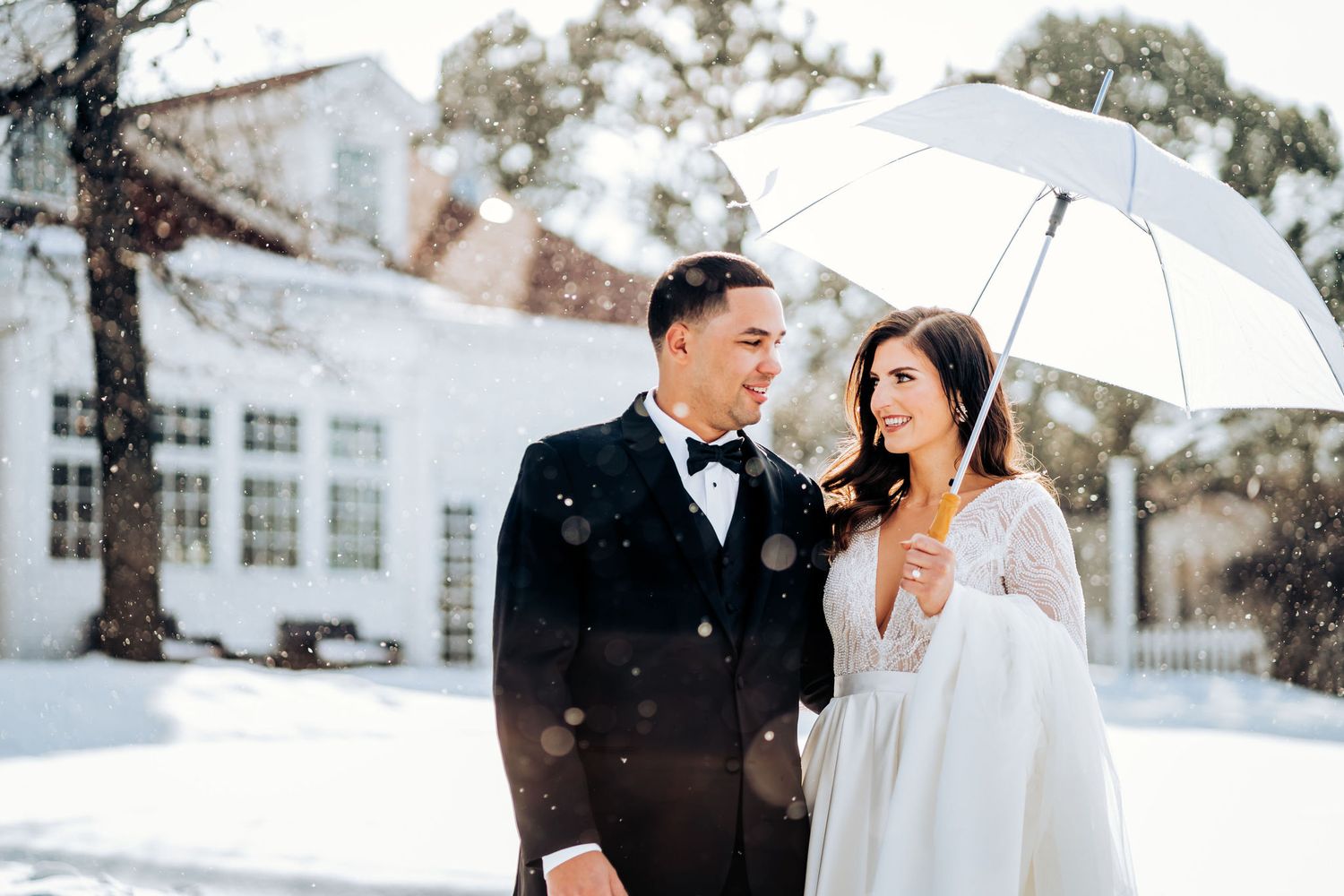 A couple shares a joyful moment under a white umbrella in the snow.