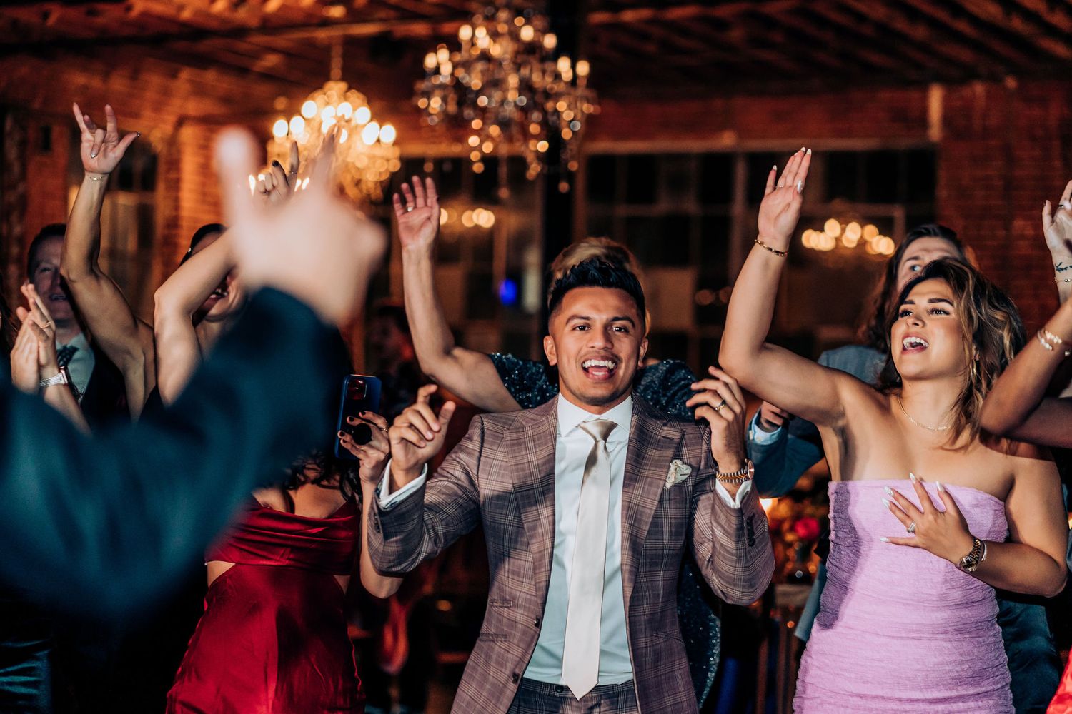Wedding guests dance and celebrate enthusiastically at an indoor reception.