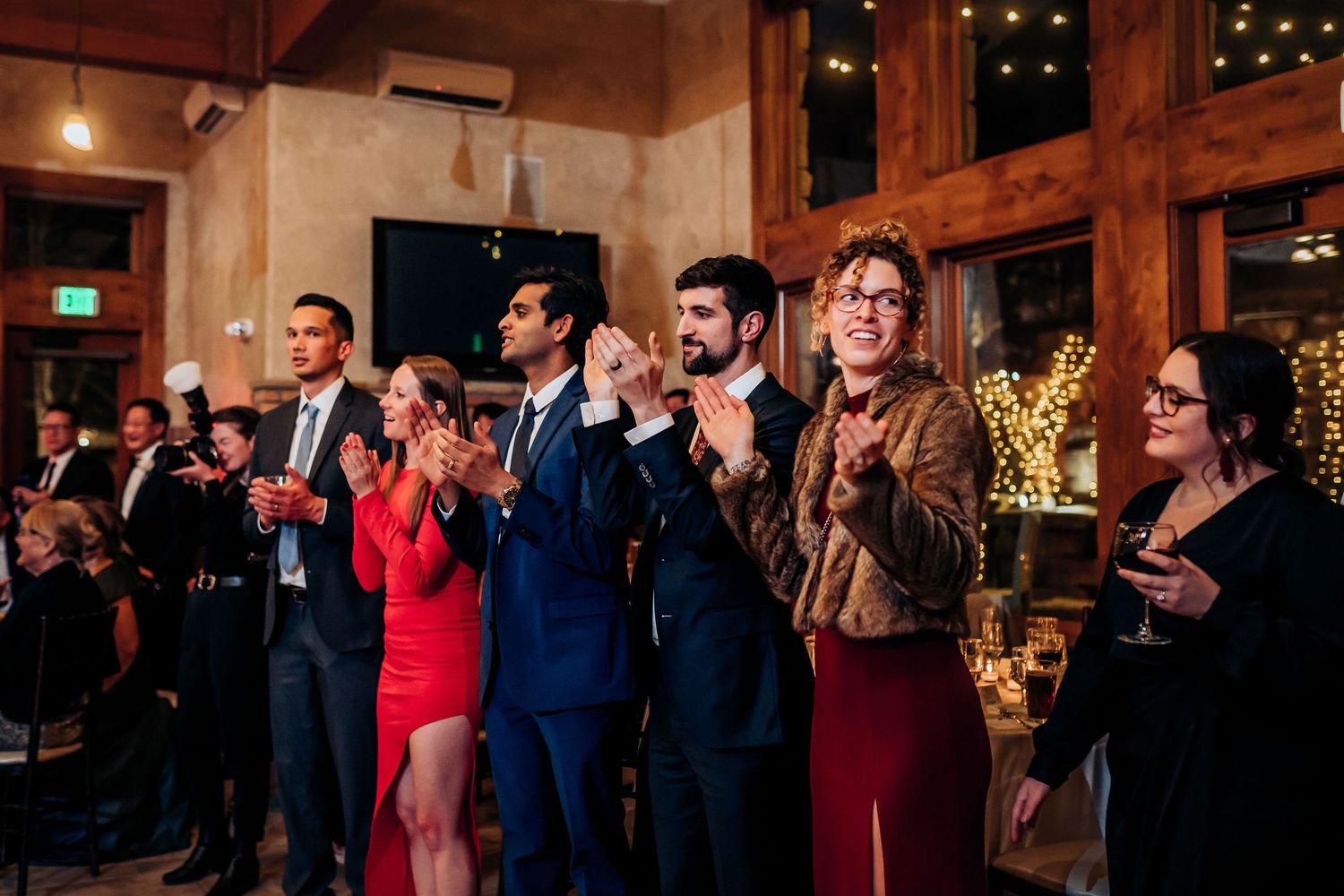 Wedding guests applaud and celebrate during reception festivities in a rustic wooden venue.