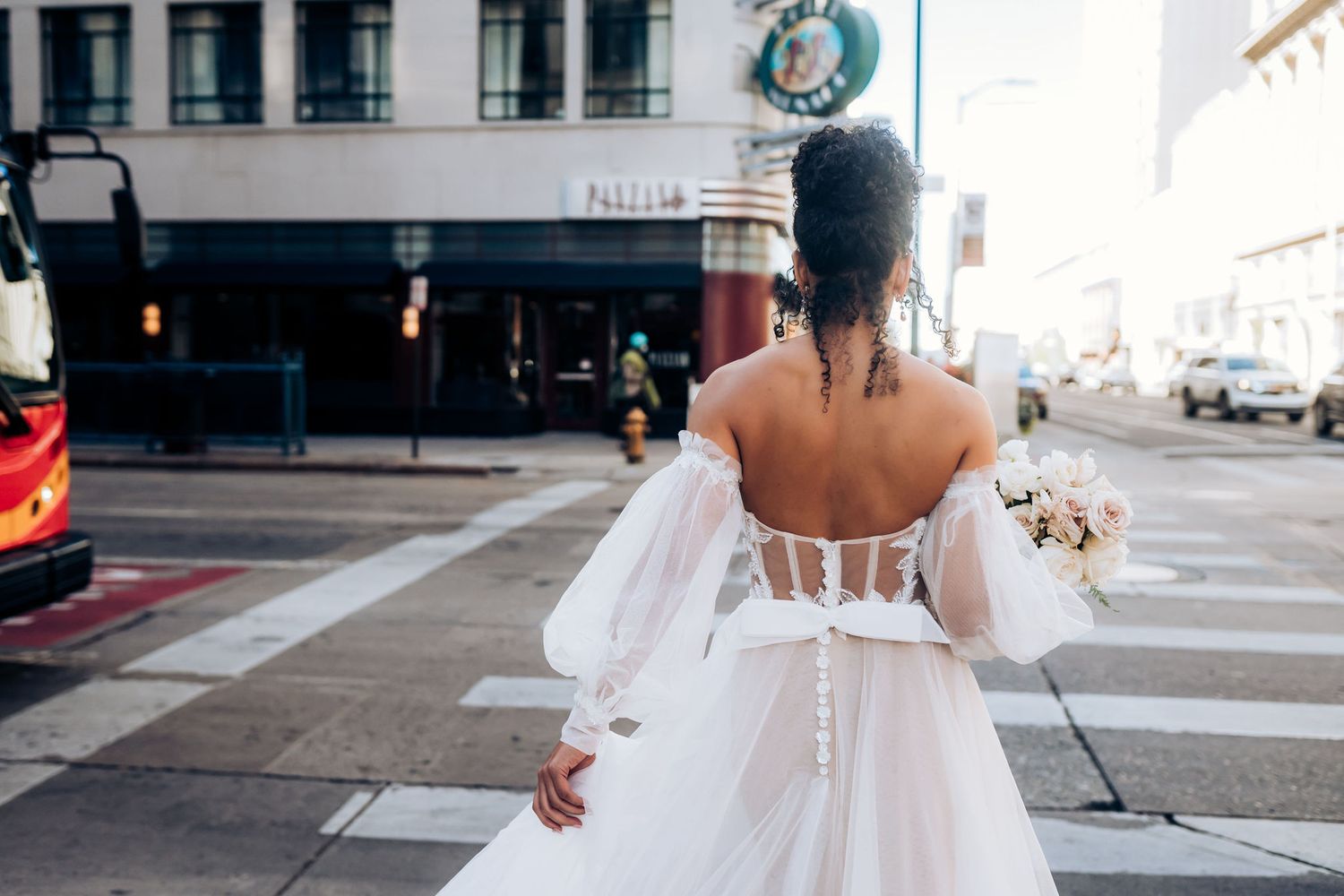 Bride in flowing white dress walking down urban street with buildings in background.