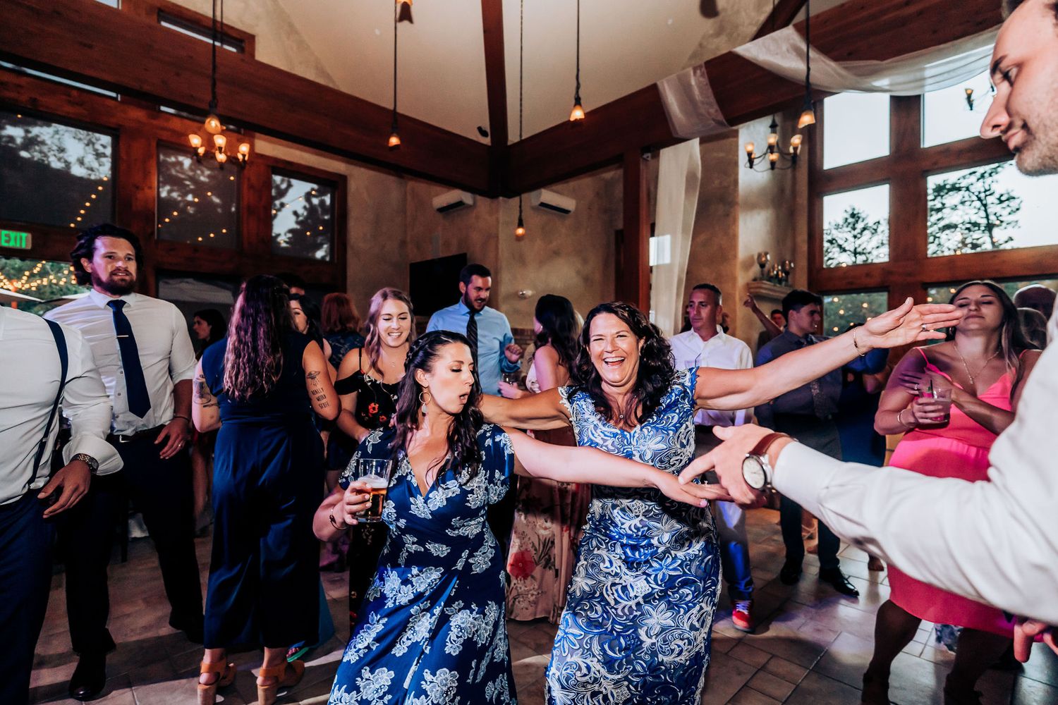 Wedding reception guests dancing and celebrating in a venue with rustic decor and natural lighting.