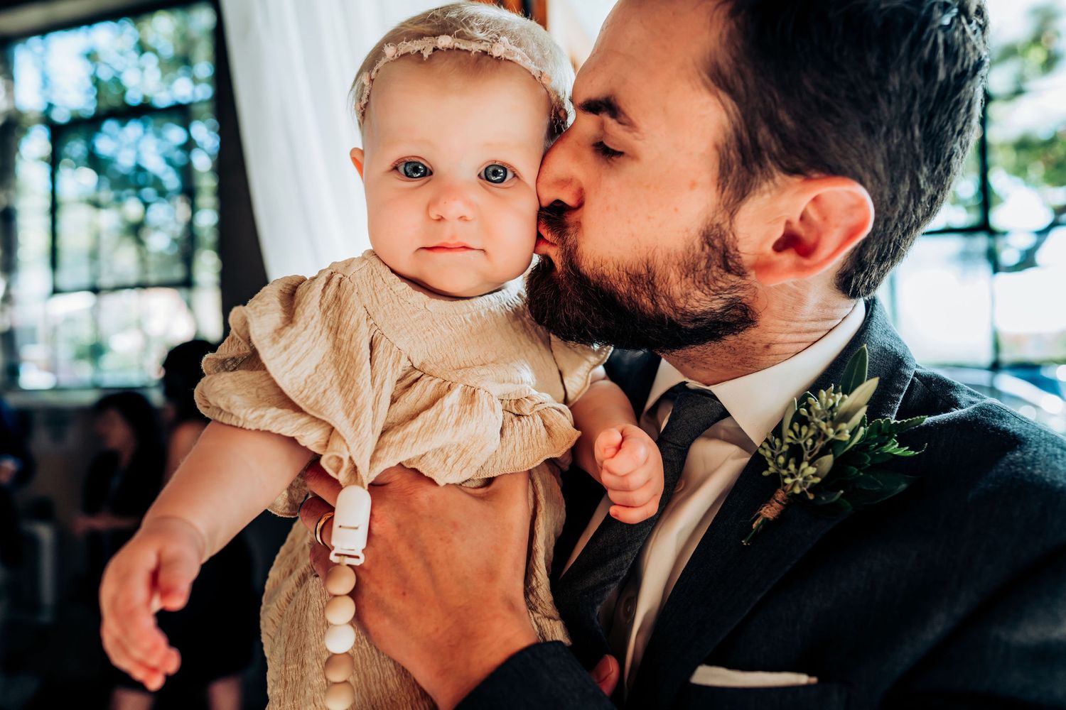 Tender moment between a person in formal wear and a baby in a cream-colored dress.