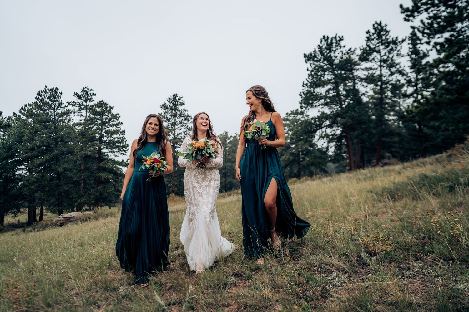 Three attendants in navy and white dresses walking together on mountain hillside.