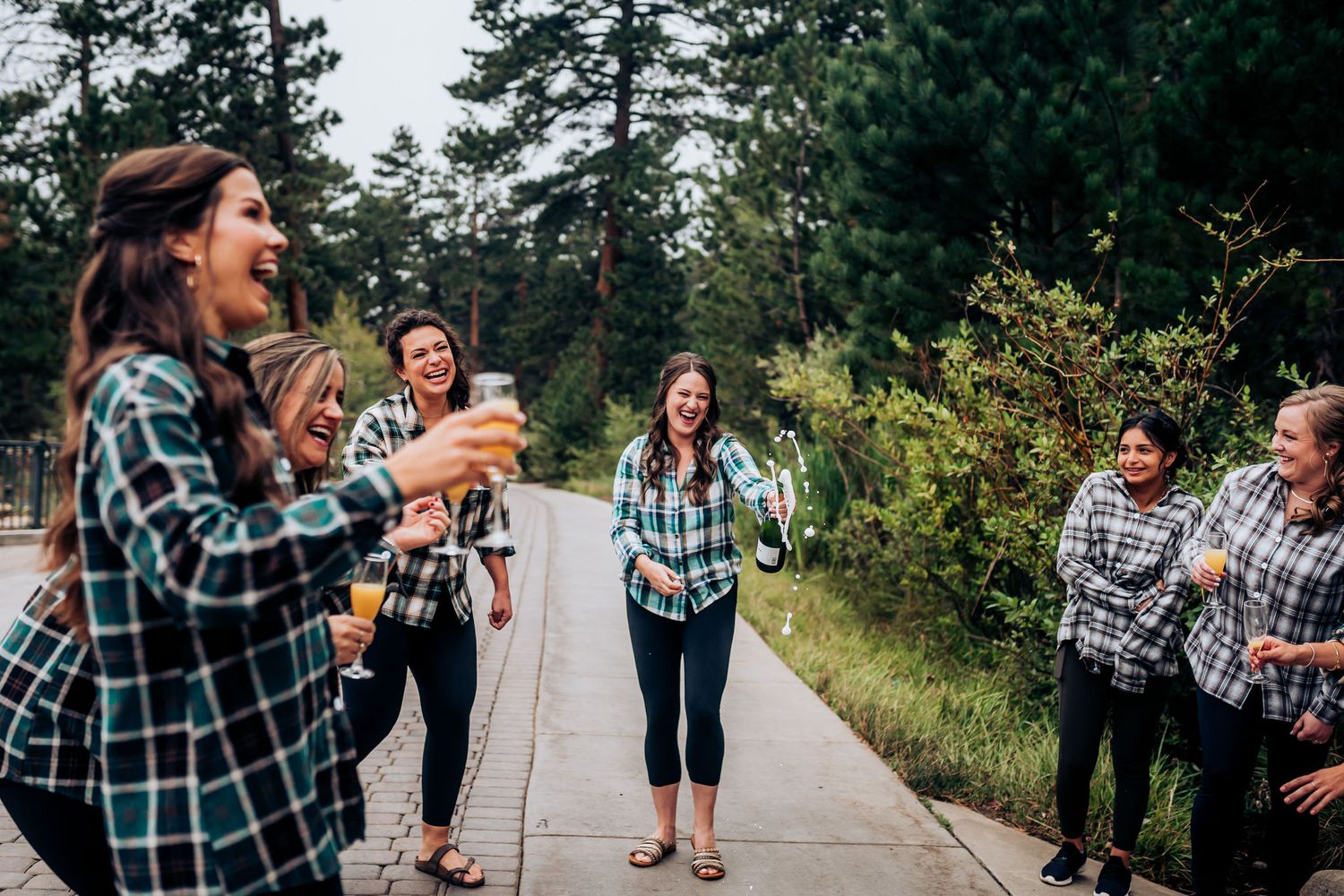 Friends in coordinated plaid shirts celebrating with drinks in a forest setting.