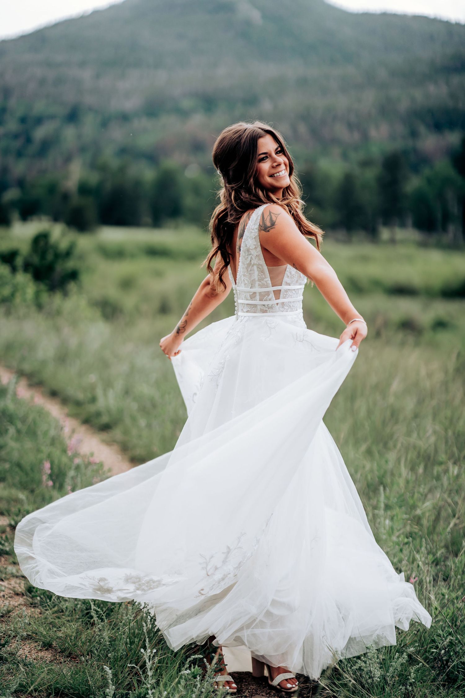 A bride twirls her flowing white wedding dress in a mountain meadow with scenic views.