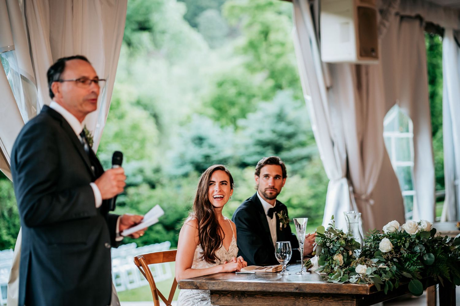 A wedding reception speech being delivered under an elegant tent with draped fabric decor.