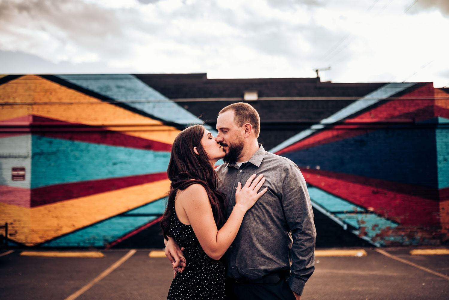 A couple embraces passionately against a backdrop of colorful geometric street art.