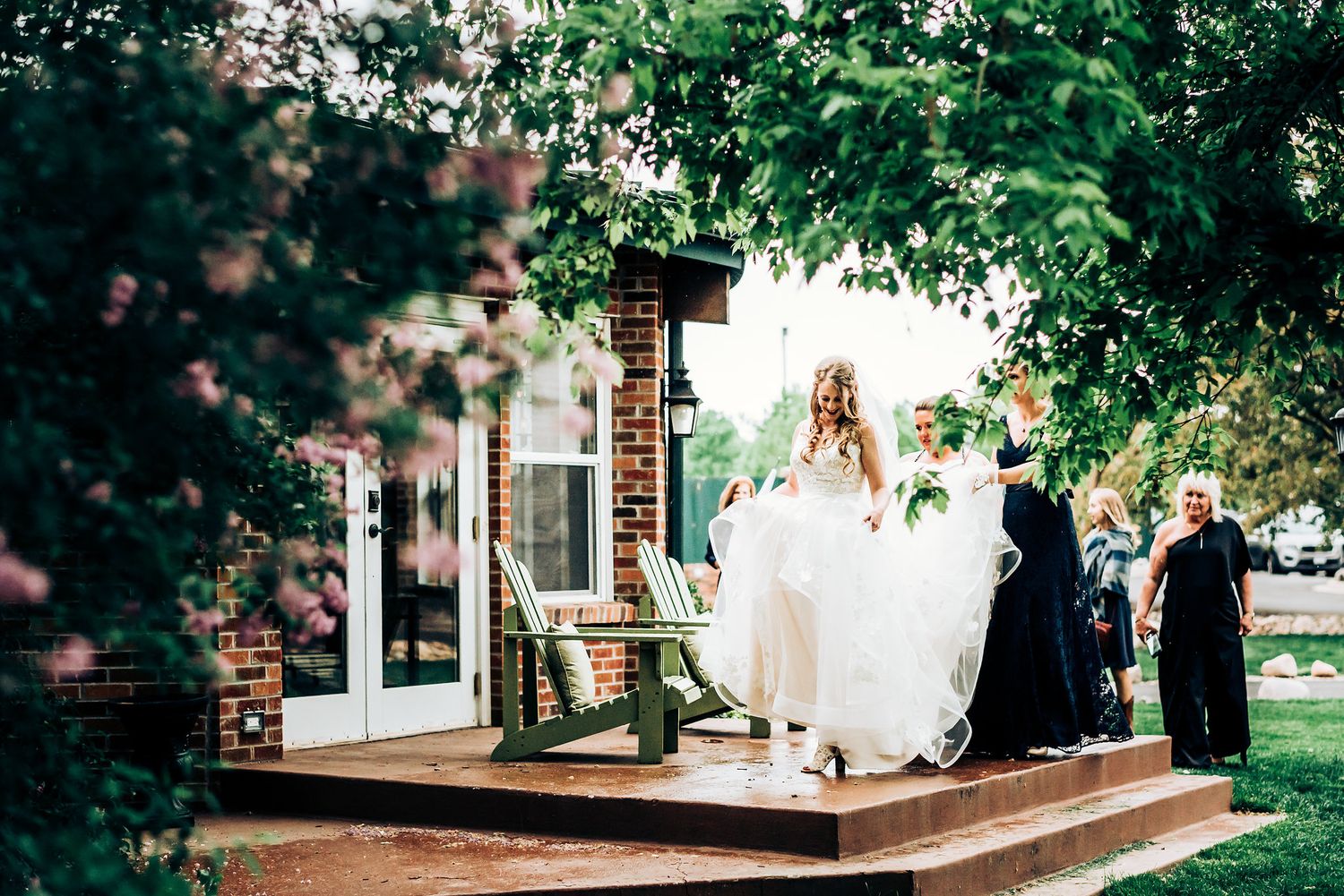 Wedding dress flowing as bride steps onto wooden deck surrounded by greenery.