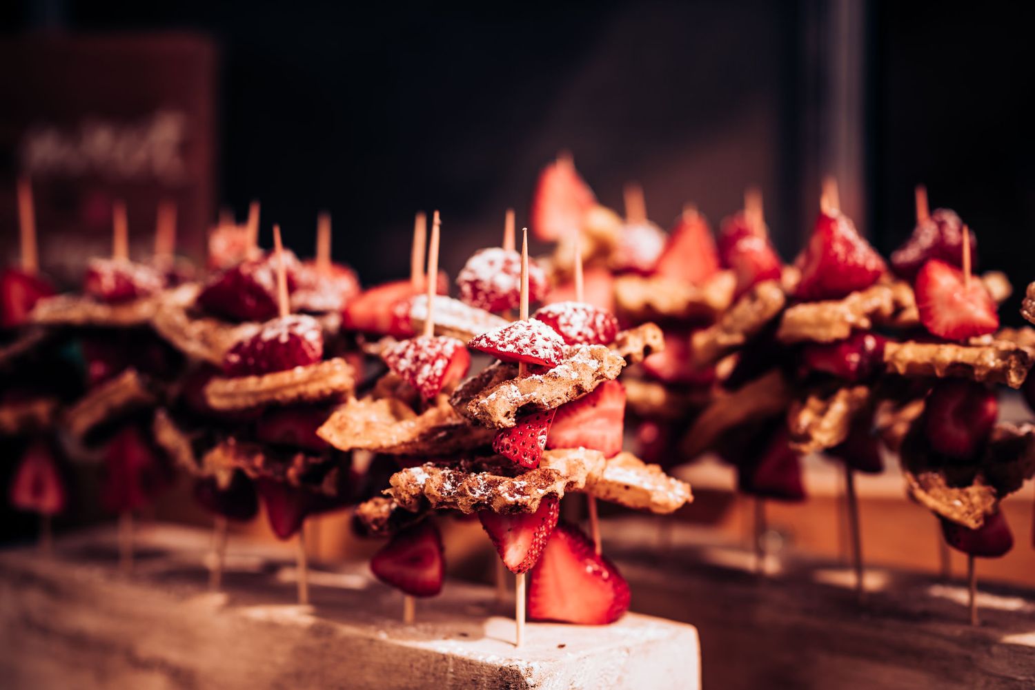 Artfully plated appetizers on wooden skewers displayed under warm lighting.