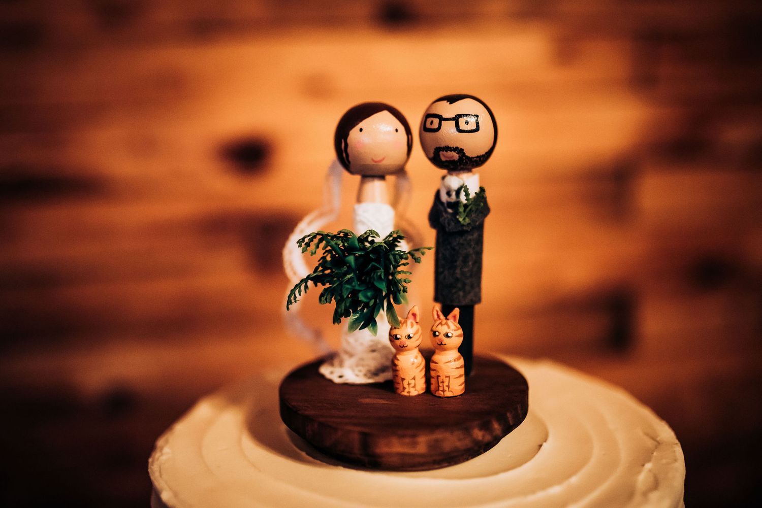 Cute wooden wedding cake topper figurines with miniature greenery on rustic display.