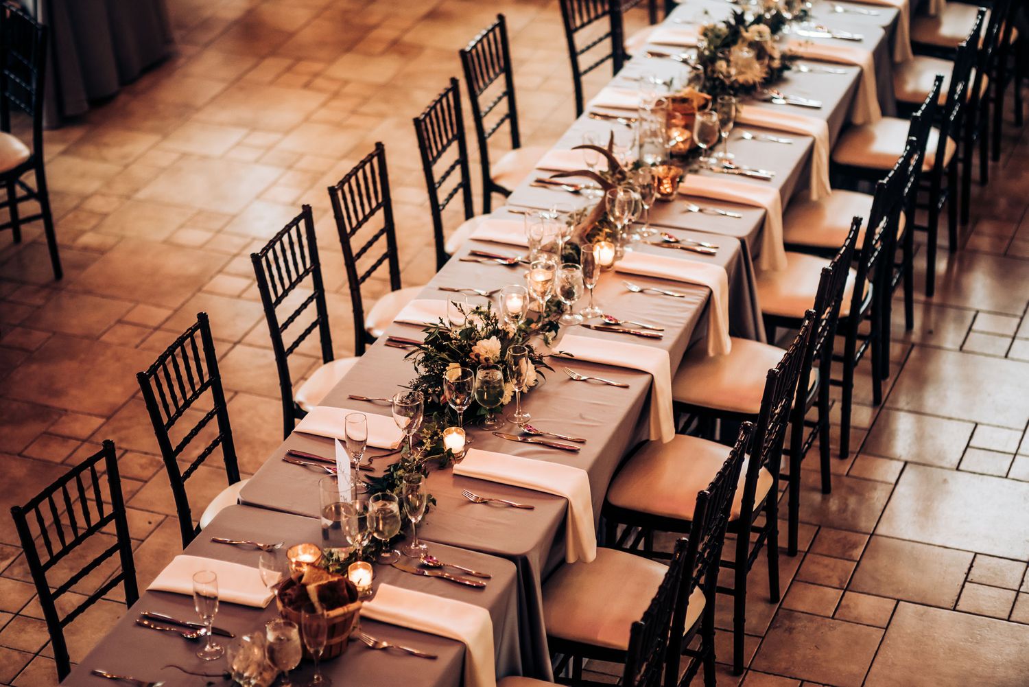 Long banquet table set for wedding with floral garland and Chiavari chairs.