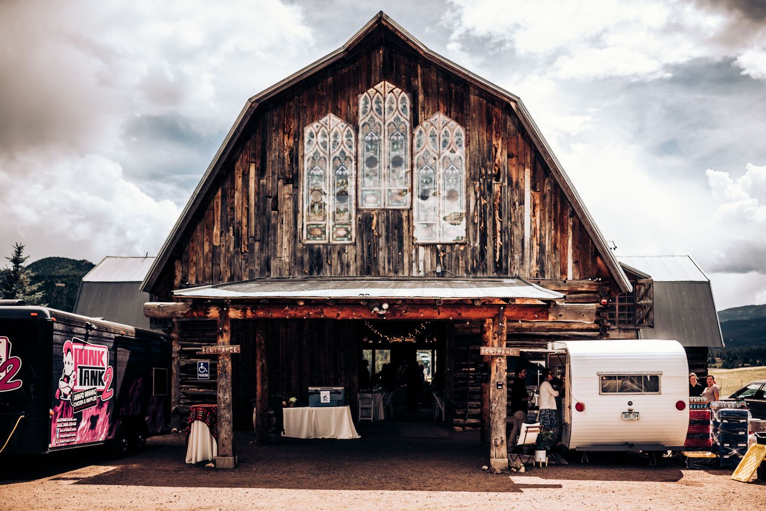 A rustic barn venue with decorative window panels and food trucks outside.
