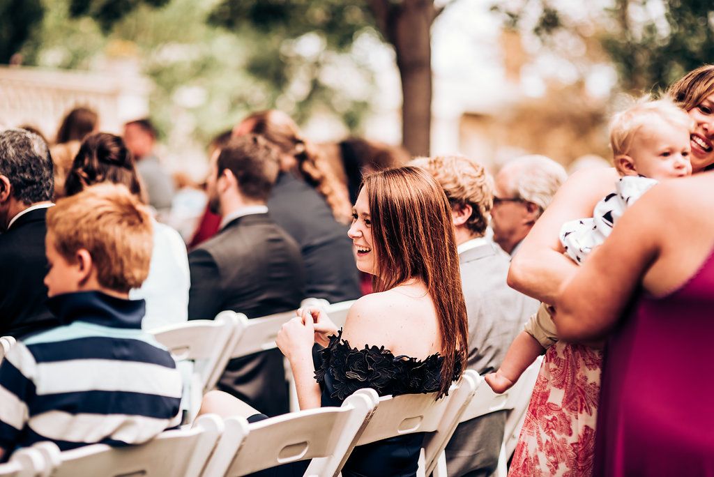 Wedding ceremony guests seated in white chairs outdoors.