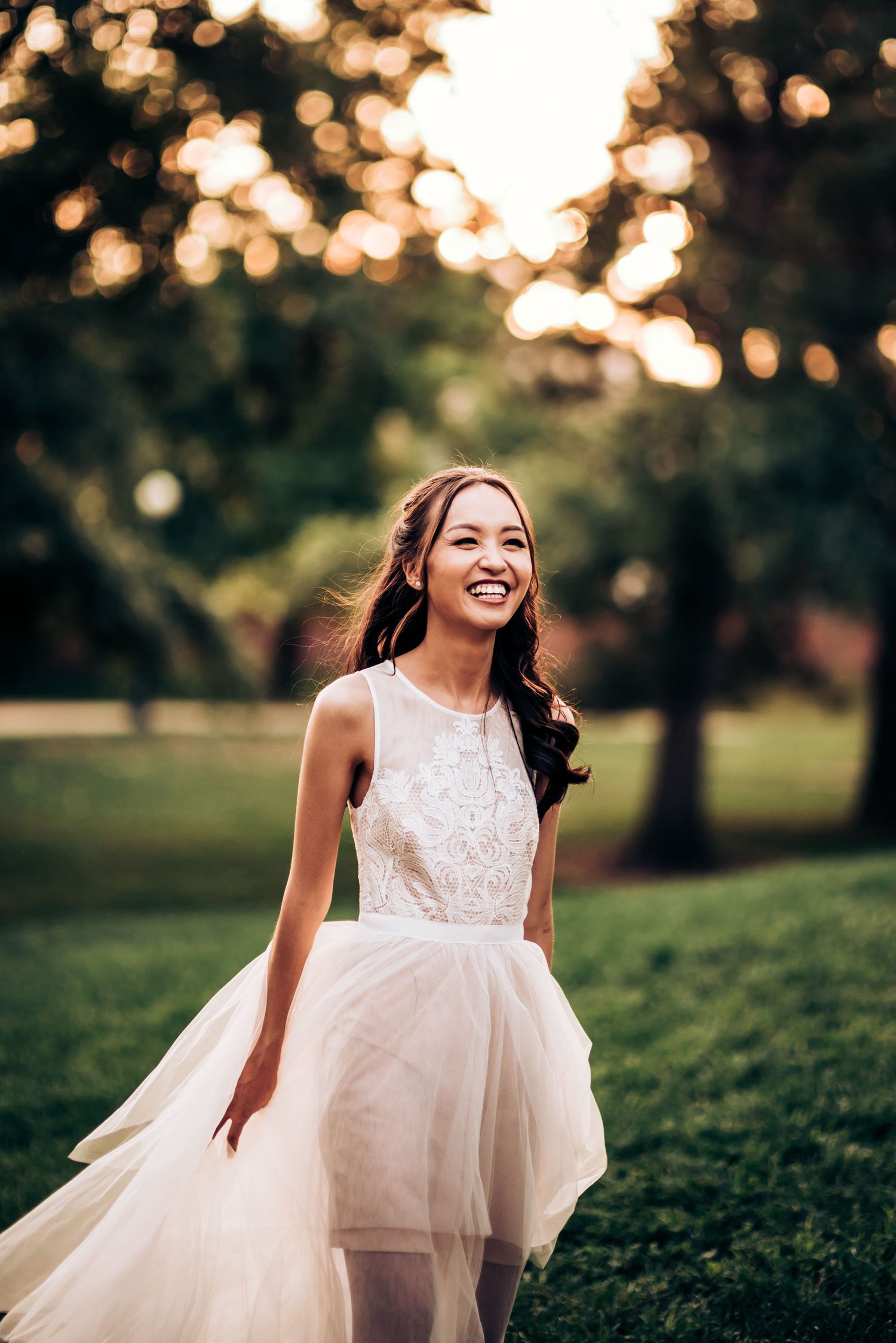A bride in a flowing tulle dress twirls in golden evening light on a grassy lawn.