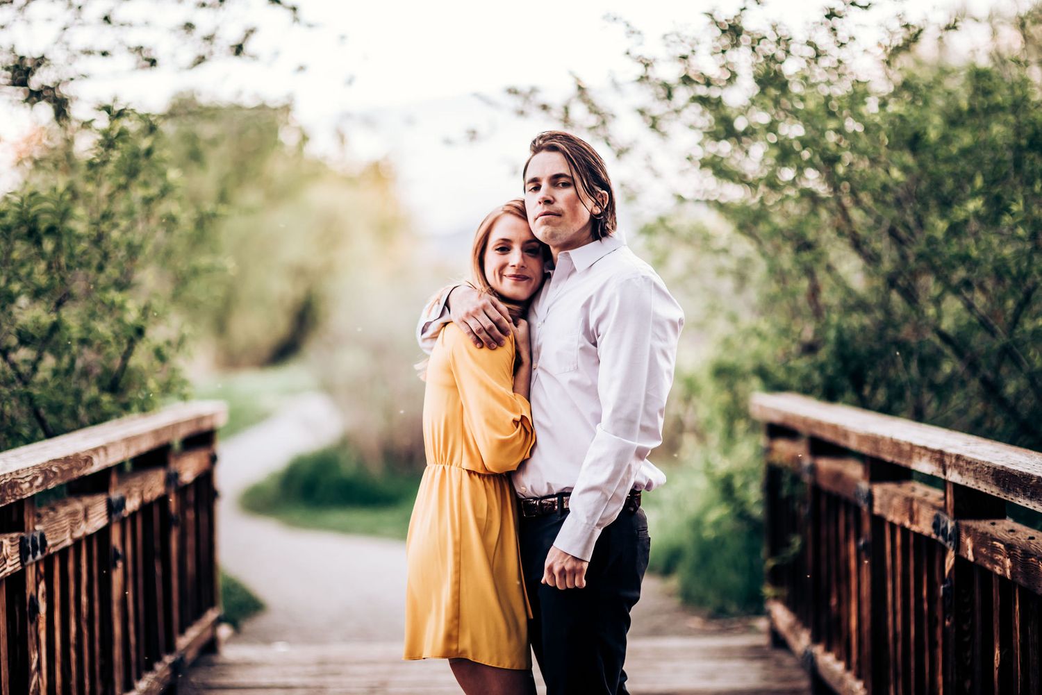 A couple poses together on a wooden bridge surrounded by lush greenery.