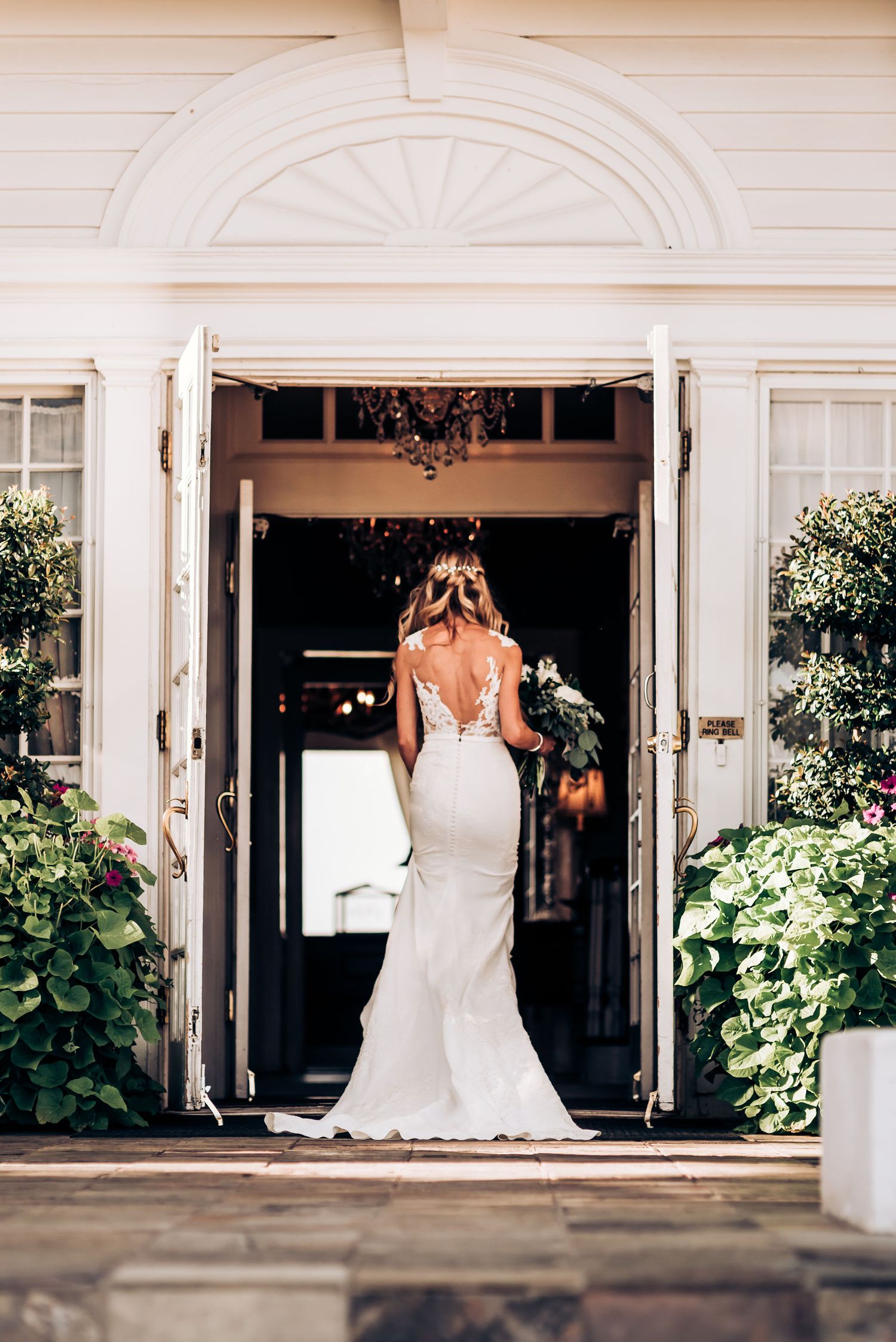 Back view of bride in fitted lace gown entering doorway of elegant white pillared building.