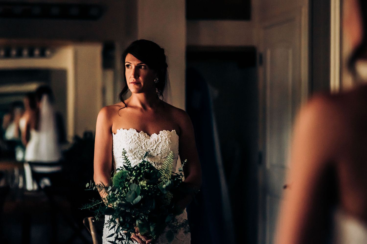 Woman in white strapless wedding gown stands in dimly lit room.