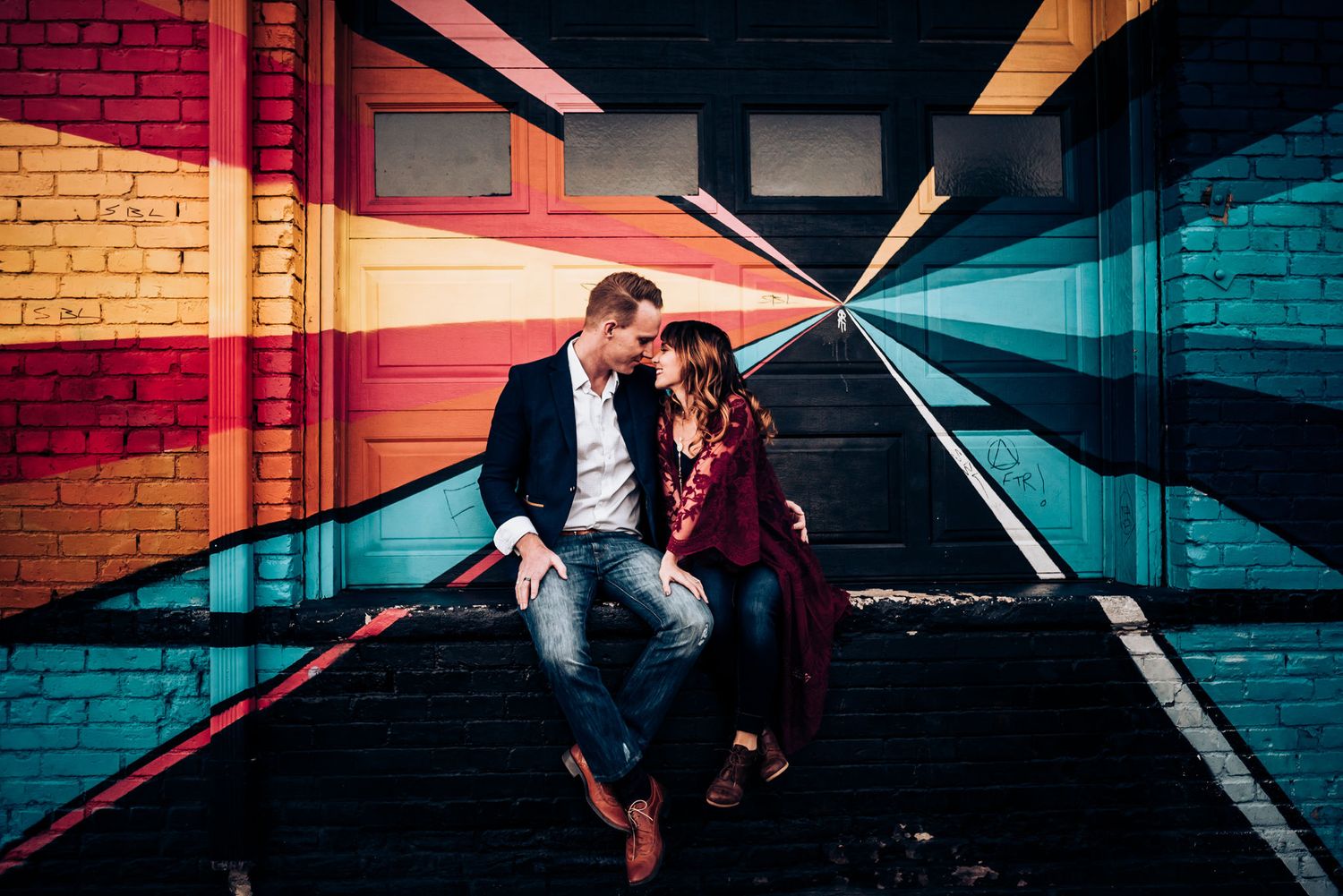A couple poses together in a vibrant hallway with geometric lighting and bold colors.