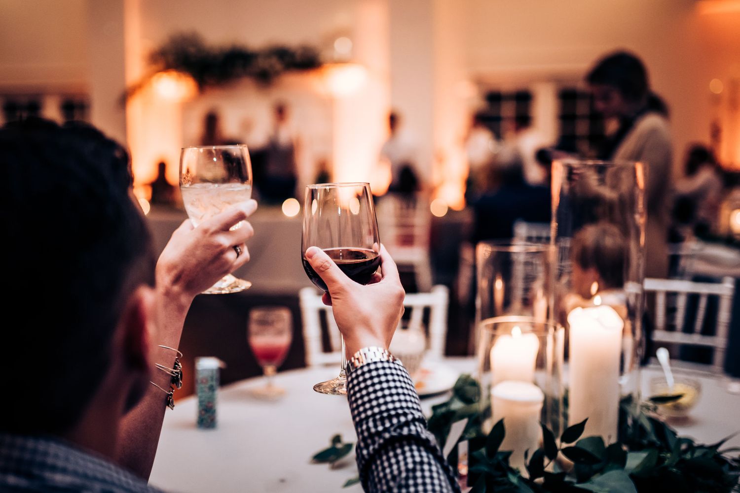 Wedding guests raise wine glasses for a toast among candlelit table settings.