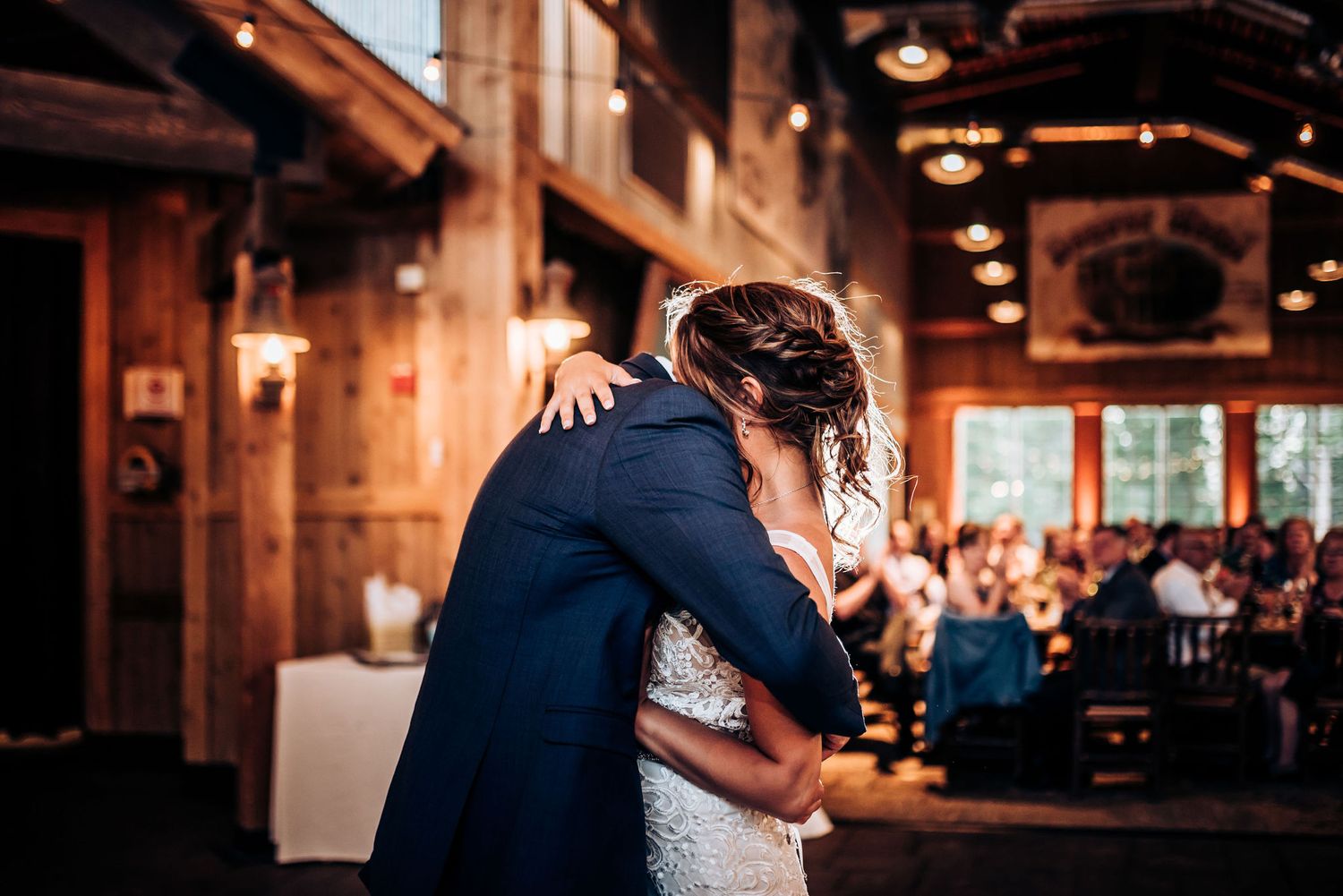 A couple embraces during their wedding dance in a warmly lit rustic venue.