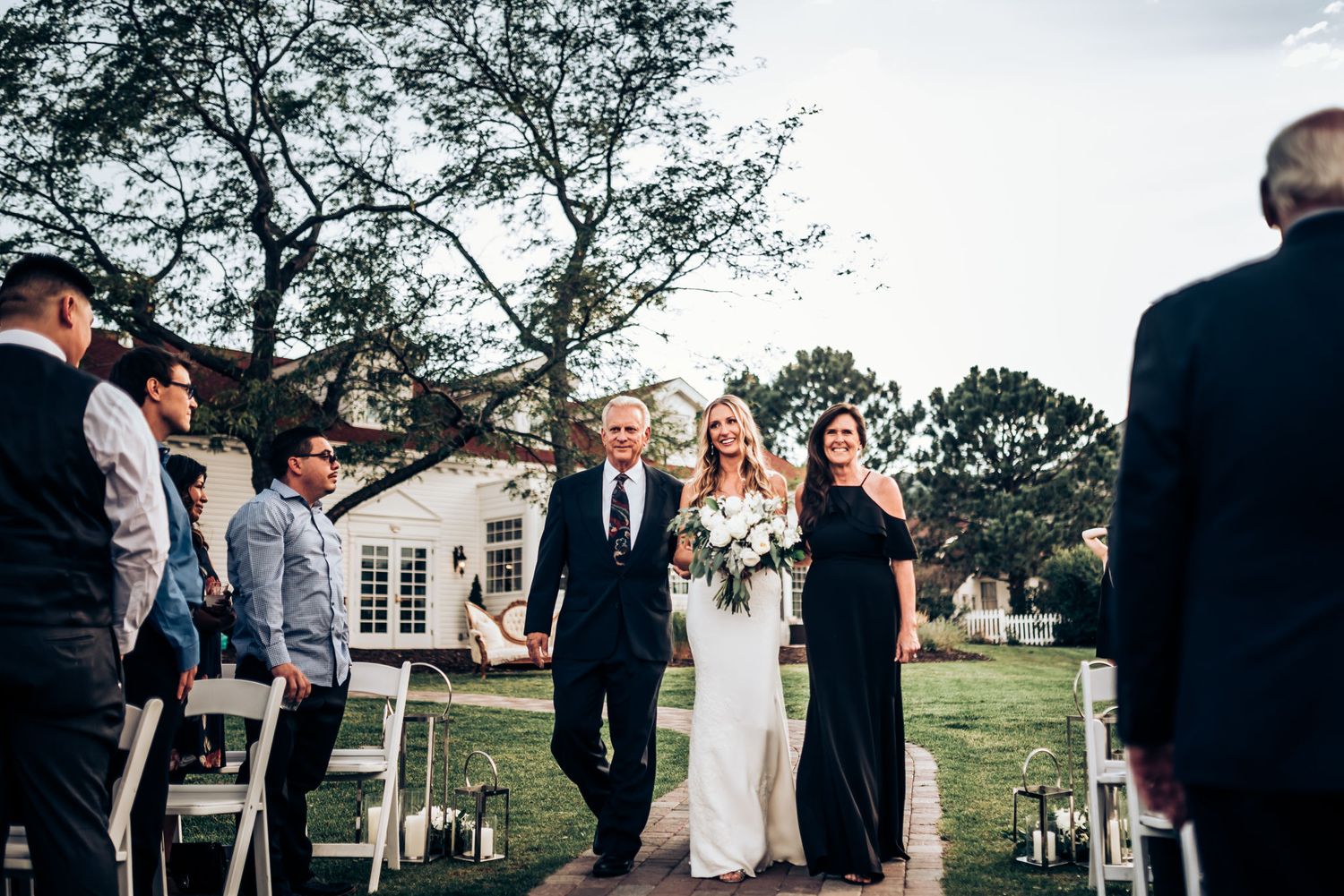 Wedding processional on lawn with white colonial style building in background.