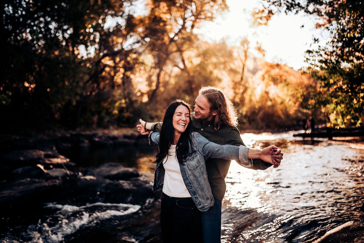 Playful couple dancing together by a rocky stream during sunset.