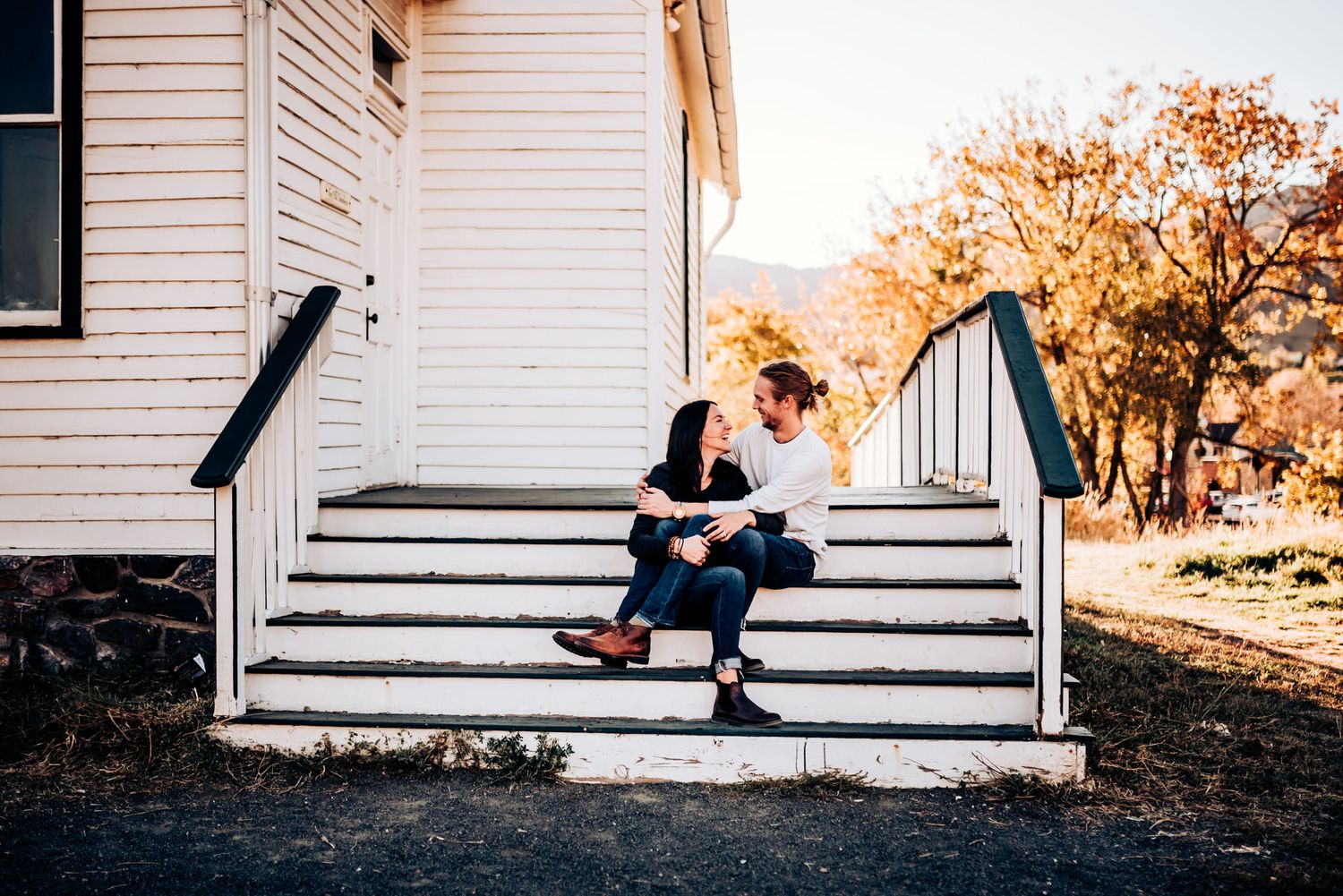 A couple shares an intimate moment on white porch steps during sunset.
