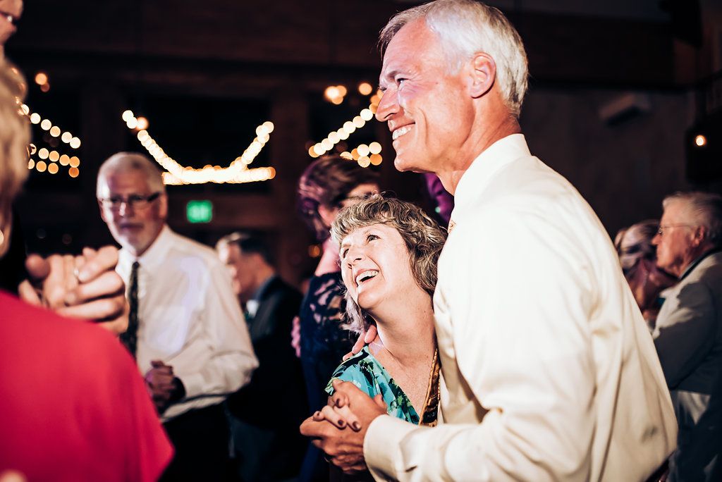 Couples dancing and laughing at a festive indoor celebration with string lights.