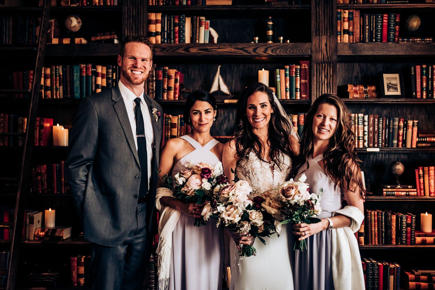 Small wedding group poses together in front of classic library backdrop with beautiful bouquets.