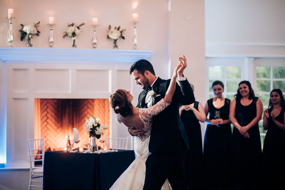Couple performs elegant dance move during wedding reception with bridesmaids watching in background.