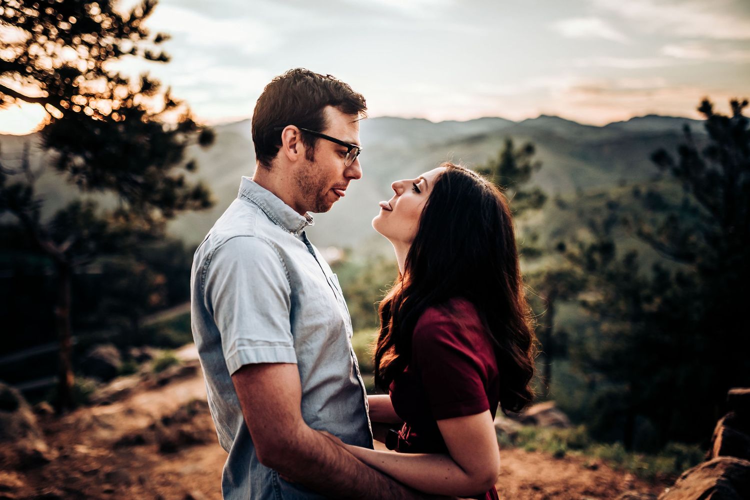 Couple sharing romantic moment on mountain overlook with scenic backdrop.