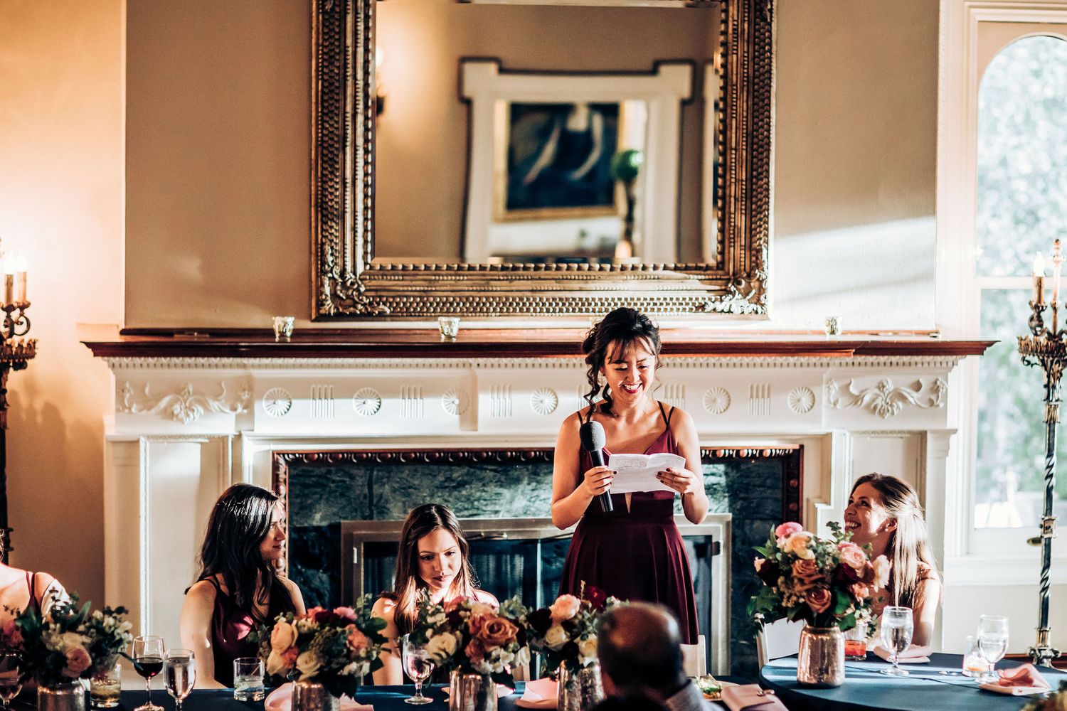 Speech being delivered during a formal dinner reception in front of an ornate fireplace.