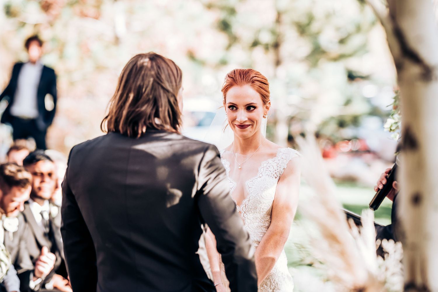A joyful moment during an outdoor wedding ceremony with autumn trees in the background.