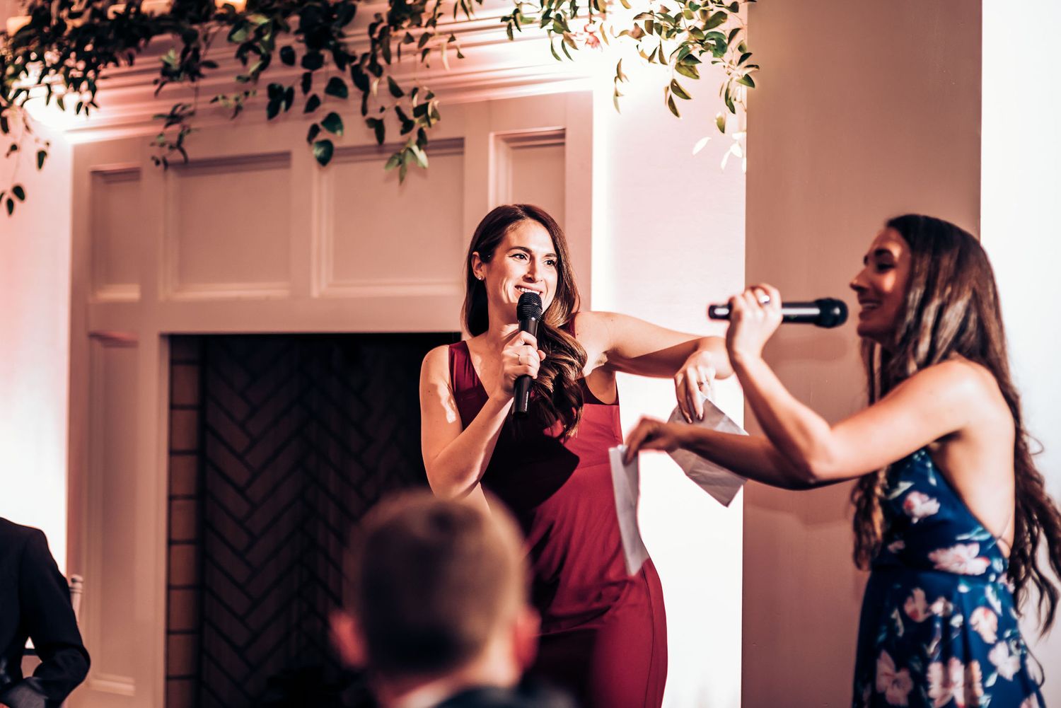 Two speakers share microphones during formal event speech with burgundy and navy attire.